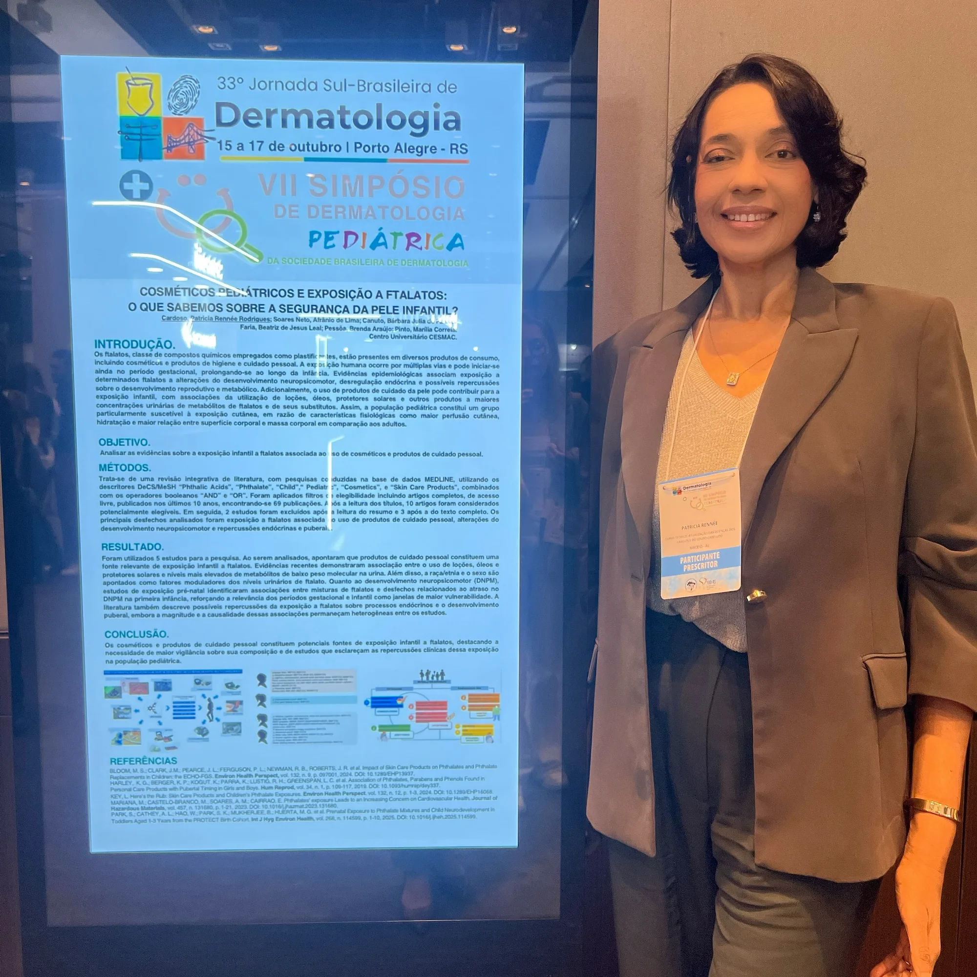 A Dra. Patricia Rennée sorri ao lado do pôster digital do trabalho sobre cosméticos pediátricos e ftalatos, na Jornada Sul-Brasileira de Dermatologia, em Porto Alegre.